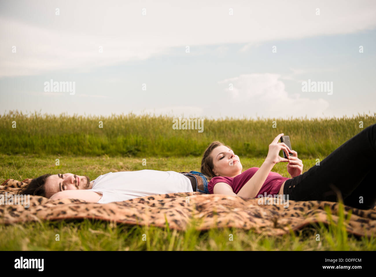 Coppia giovane rilassante all'aperto in natura - donna con lo smartphone si trova sull'uomo Foto Stock