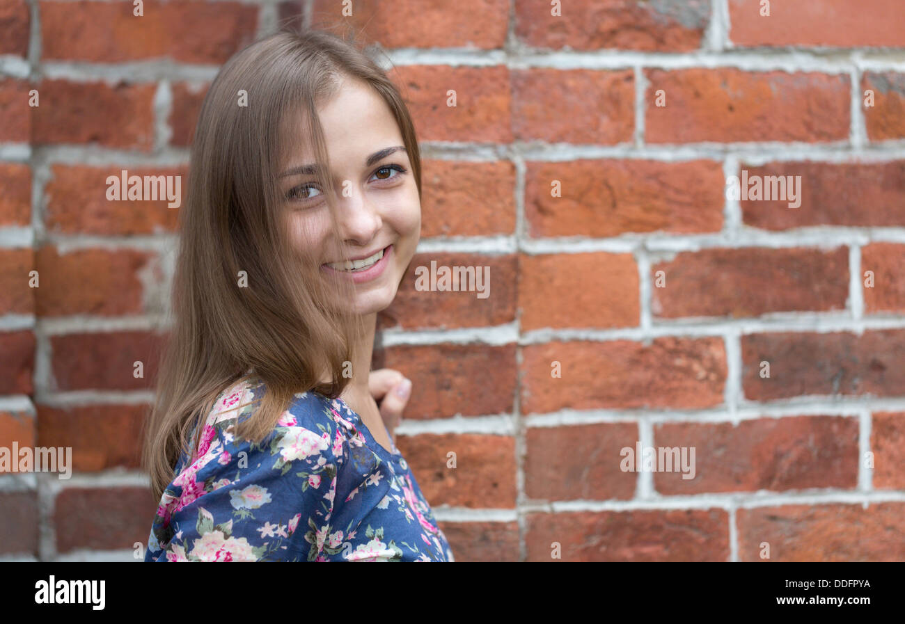 Ritratto di una giovane e bella ragazza su uno sfondo di mattoni rossi. Foto Stock