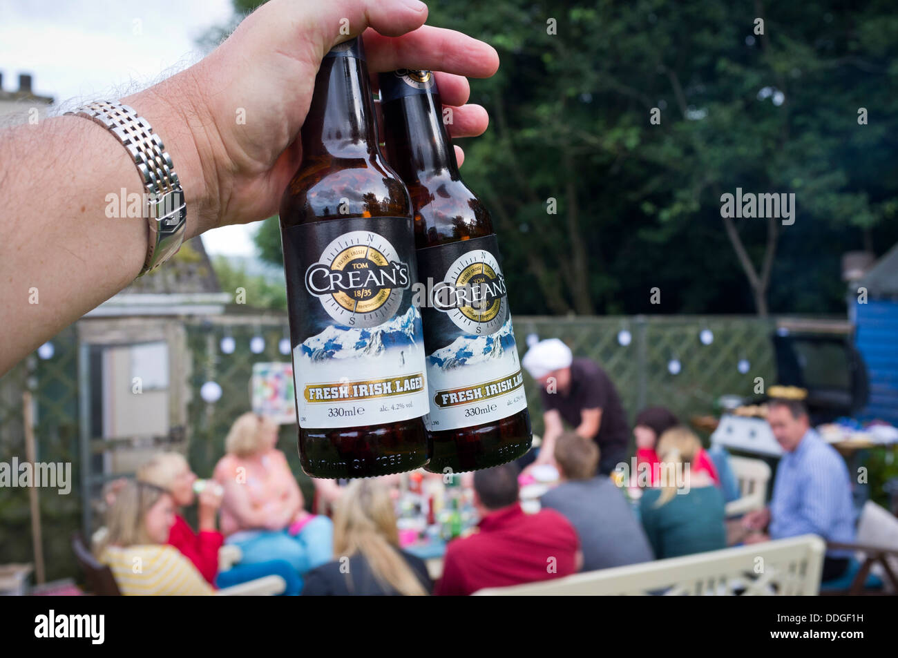 Due bottiglie di birra lager Creans detenute aloft presso un giardino esterno parte Foto Stock