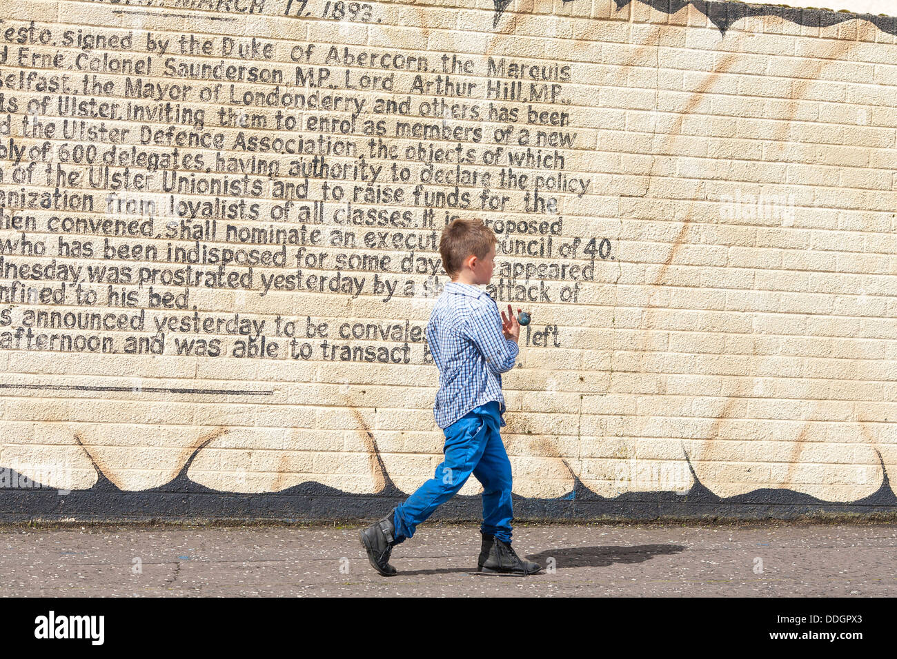 Un giovane scolaro passeggiate da un murale di politici che adorna le pareti delle case in occidente protestante di Belfast Foto Stock