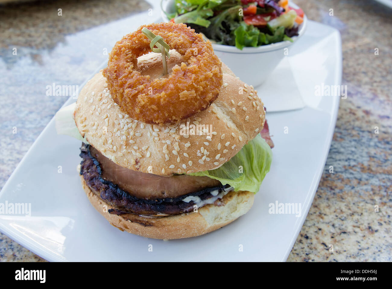 Hamburger con anello di cipolla prosciutto polpetta di carne bovina la lattuga e una ciotola di organico insalata verde Foto Stock