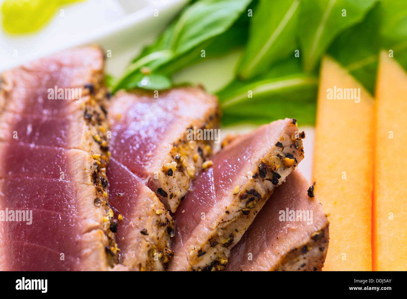 Fette di bistecca di tonno con salsa di soia, wasabi, rucola e cantalope sulla piastra, close up Foto Stock