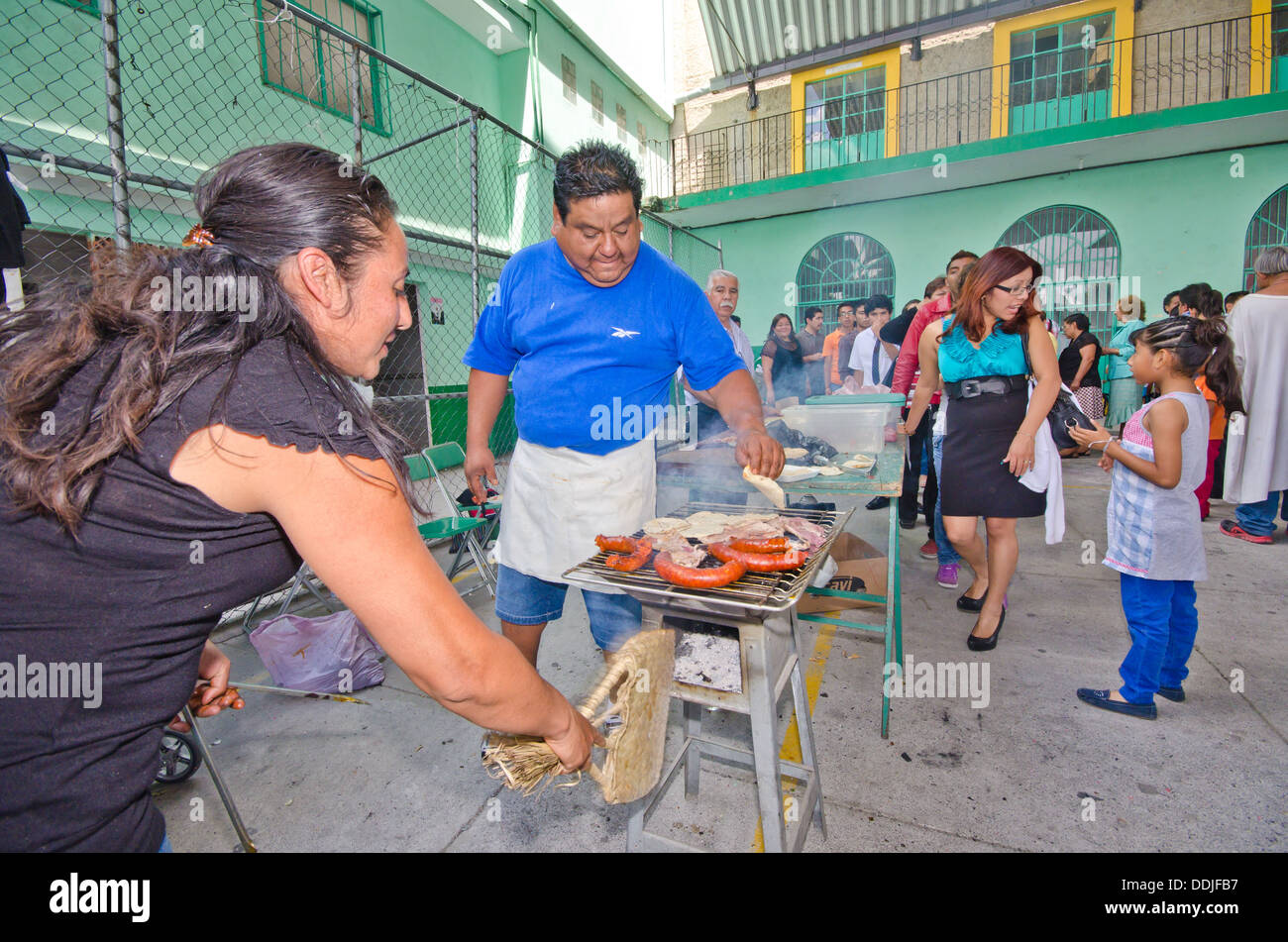 Una donna fanning le fiamme mentre l'uomo grigliate lungo il chorizo messicano di salsicce e carne al food festival Foto Stock