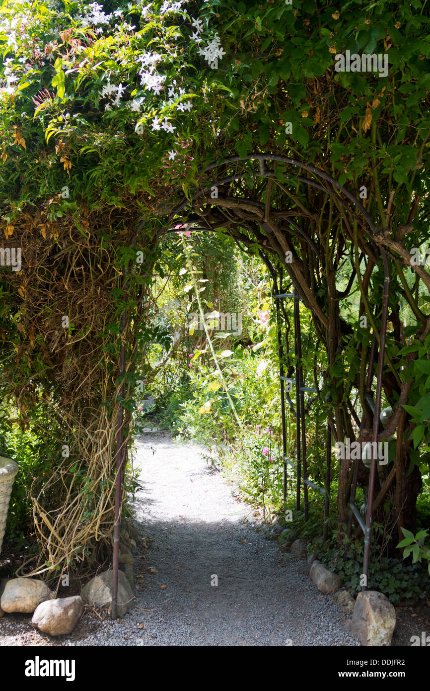 Arbor arco che conduce al giardino lussureggiante lungo il sentiero di ghiaia. Foto Stock
