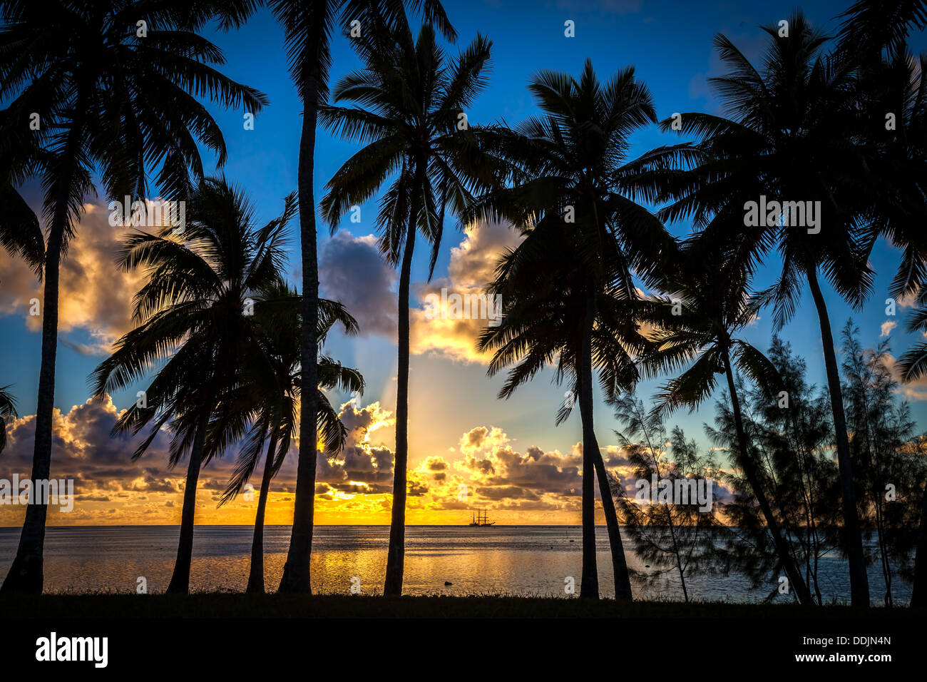 Isole di Cook, isola di Aitutaki, tramonto tropicale colori Amuri in spiaggia con una silhouette di palme che incornicia un Tall Ship Foto Stock