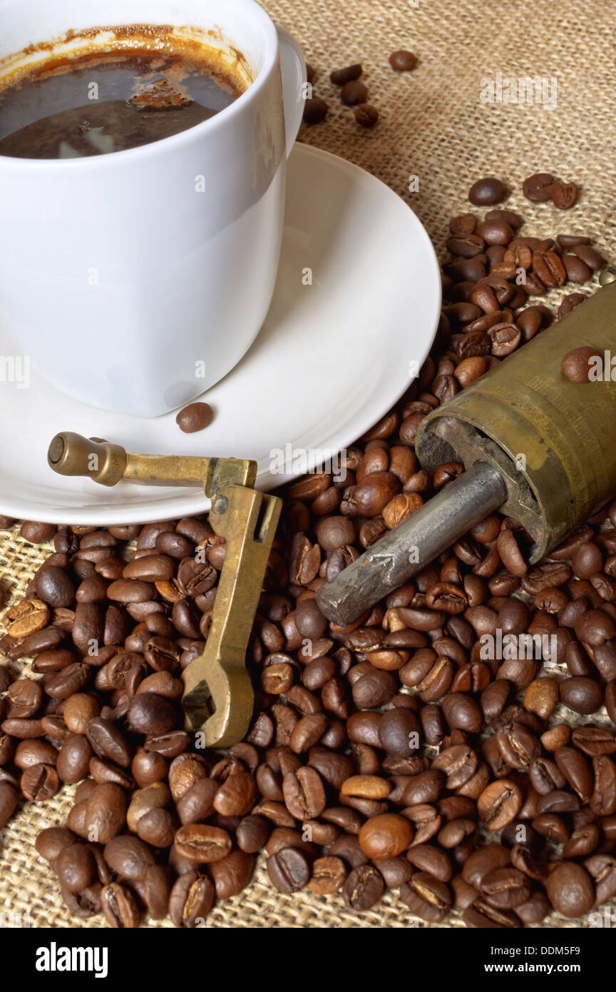 Semi di caffè con un macinacaffè e una tazza di caffè sulla tela marrone. Foto Stock