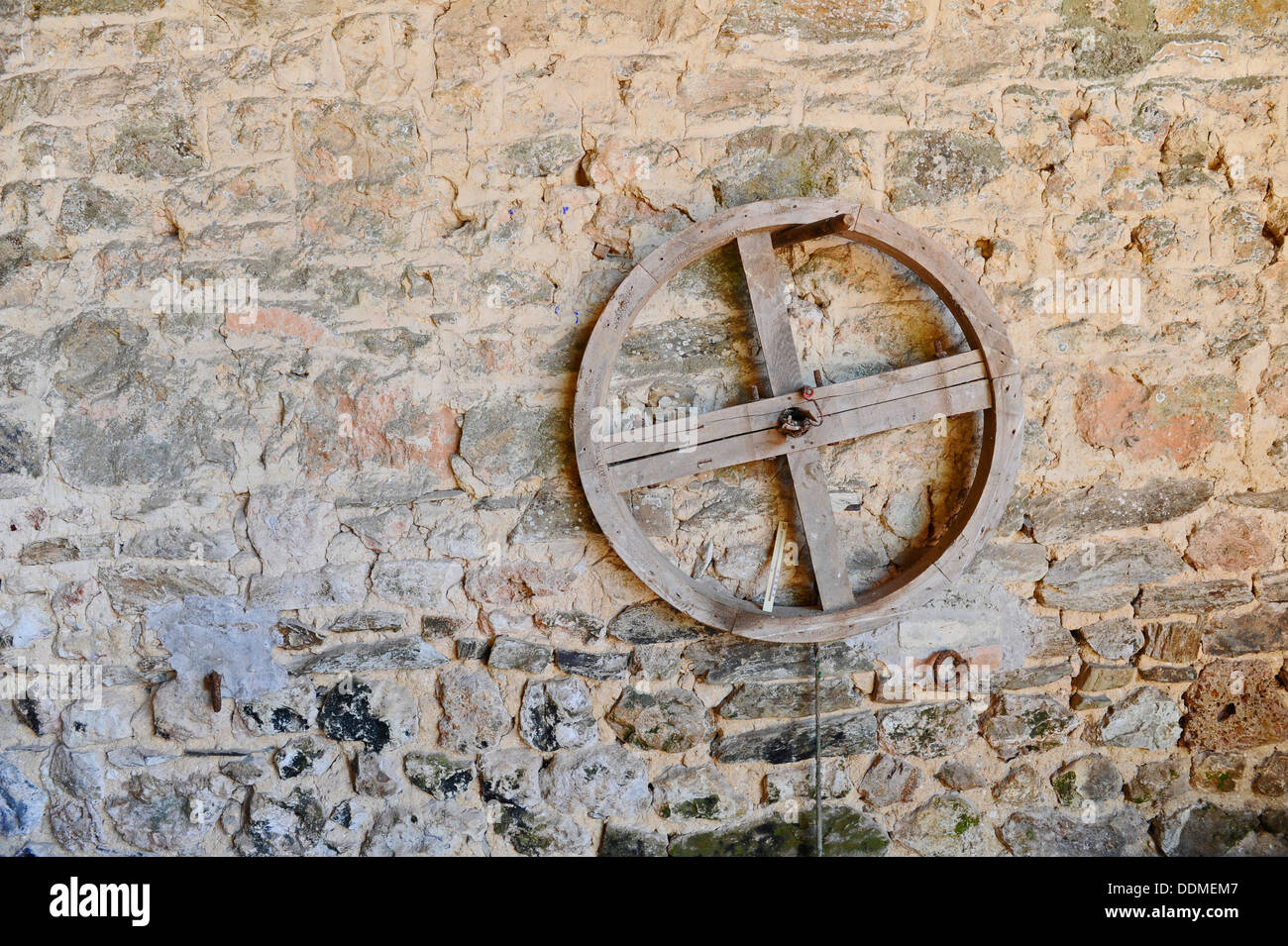 Ruota in legno pendenti da un piolino metallico attaccato a un muro di pietra in stile francese fienile. Foto Stock