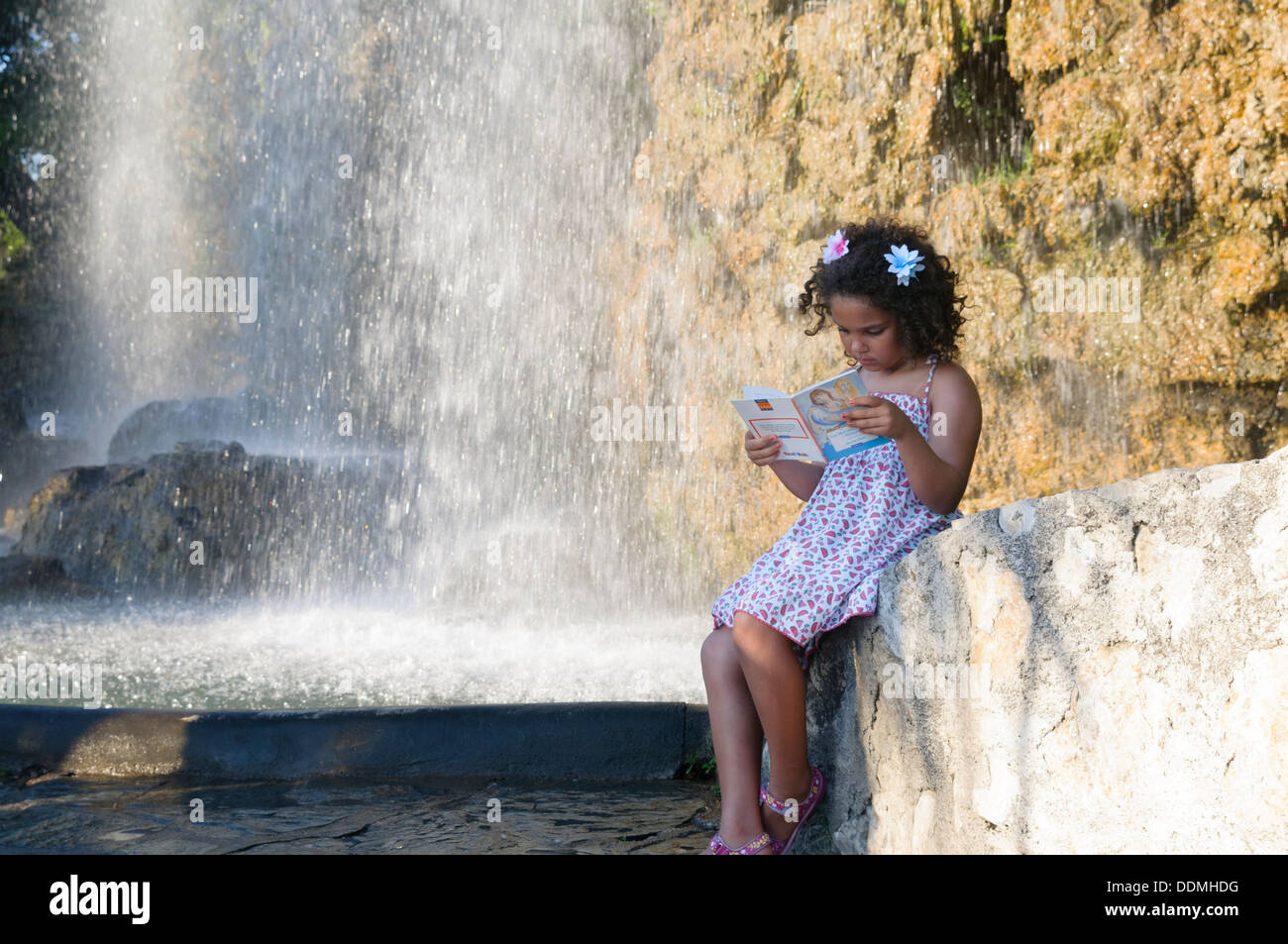 Bambina è la lettura di un libro di cascata durante il tardo pomeriggio di un giorno di estate Foto Stock