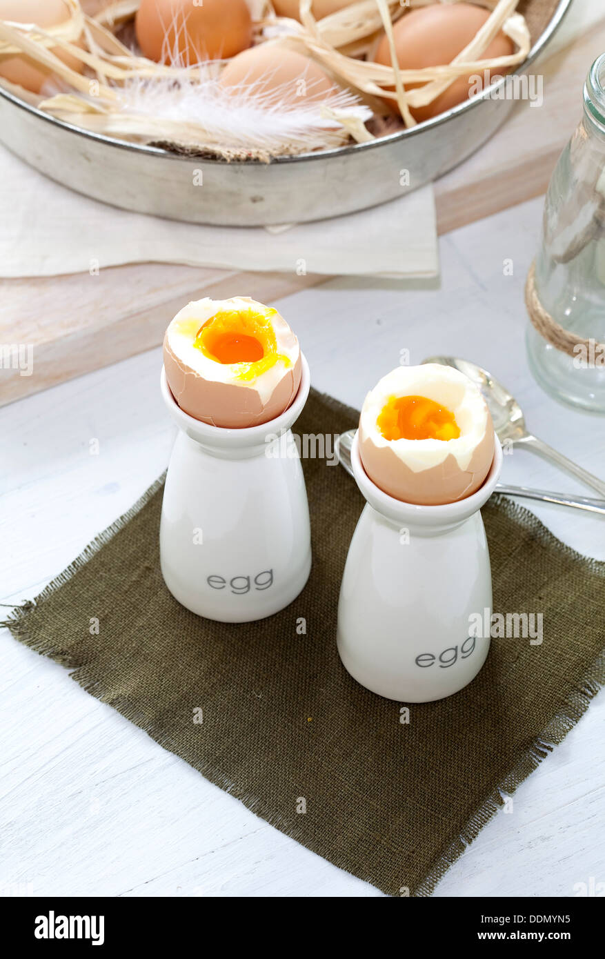 Due uova sode in coppe di uovo accanto a una ciotola di uova fresche. Foto Stock