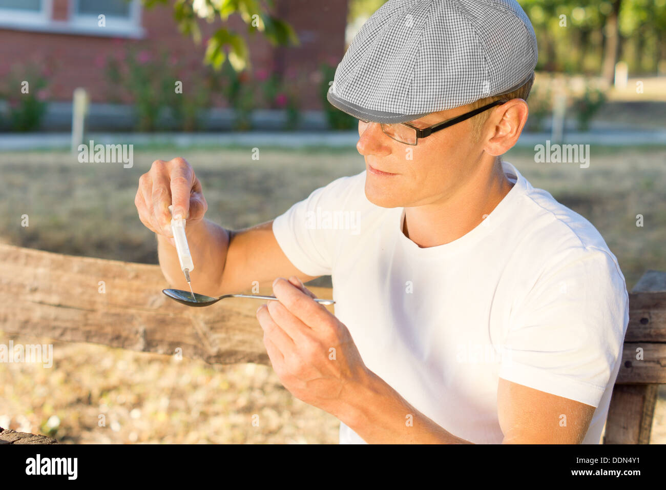 Uomo caucasico indossare una T-shirt bianco e un tappo di riempimento di una siringa con eroina iniettabile Foto Stock