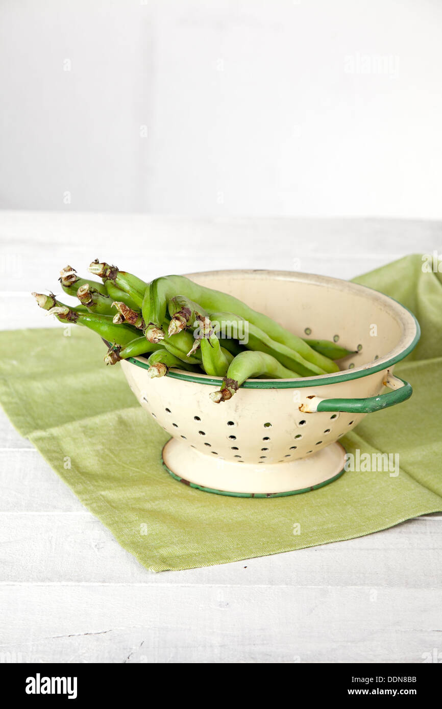 Un colapasta pieno di ampio freschi Fagioli baccelli su un tè verde e asciugamano bianco tavola di legno. Foto Stock