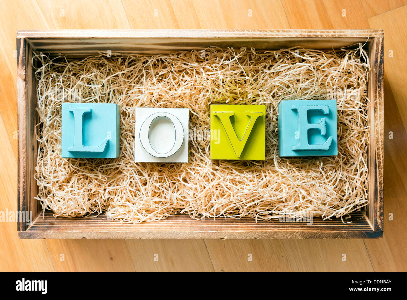 La parola amore enunciato nel grande blocco lettere in un regalo in legno scatola riempita con la rafia Foto Stock