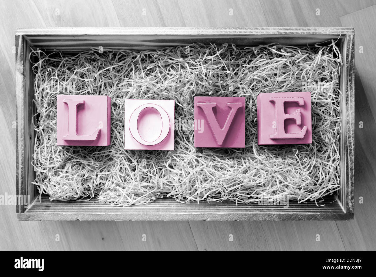 La parola amore enunciato nel grande blocco lettere in un regalo in legno scatola riempita con la rafia Foto Stock