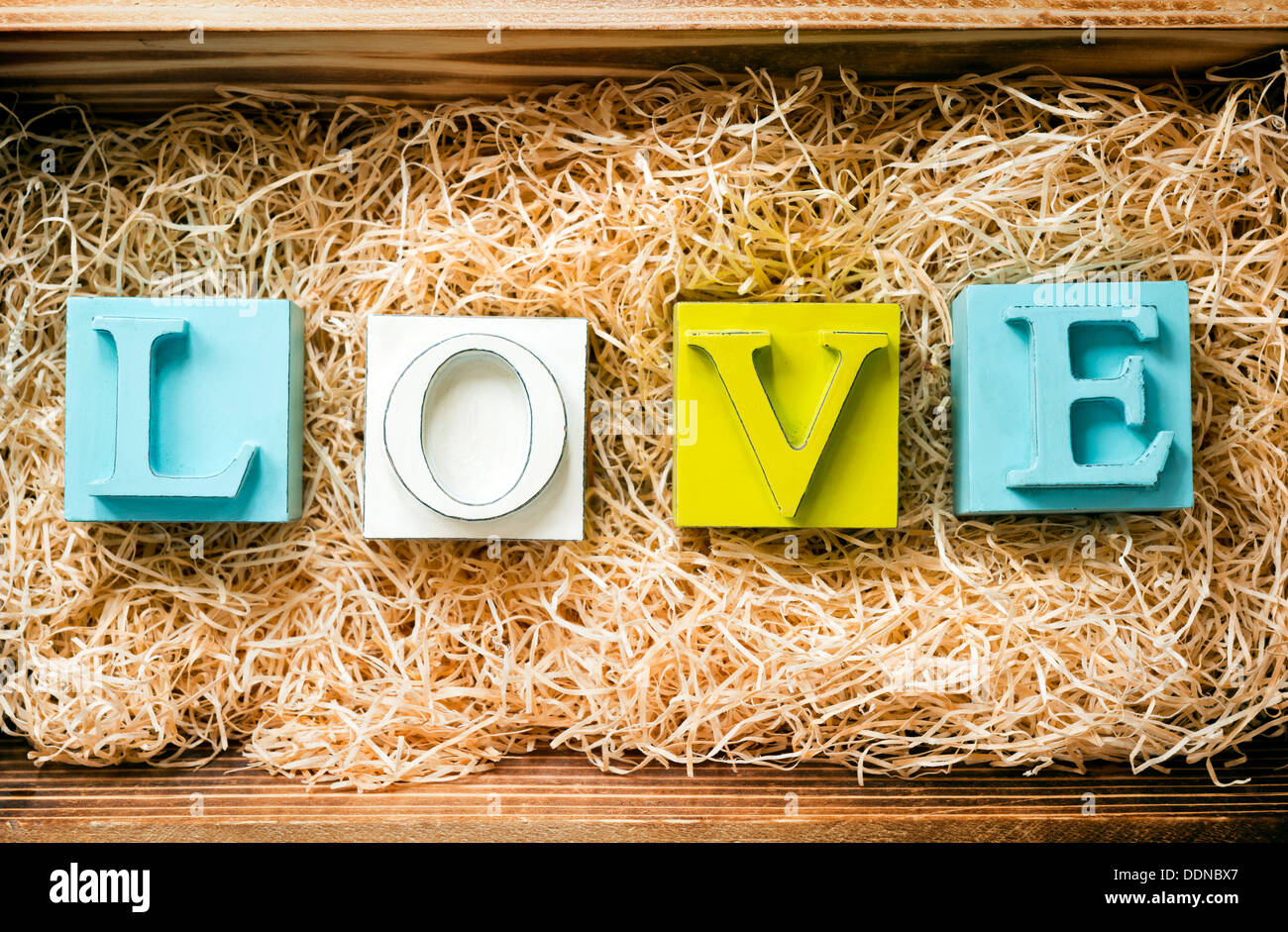 La parola amore enunciato nel grande blocco lettere in un regalo in legno scatola riempita con la rafia Foto Stock