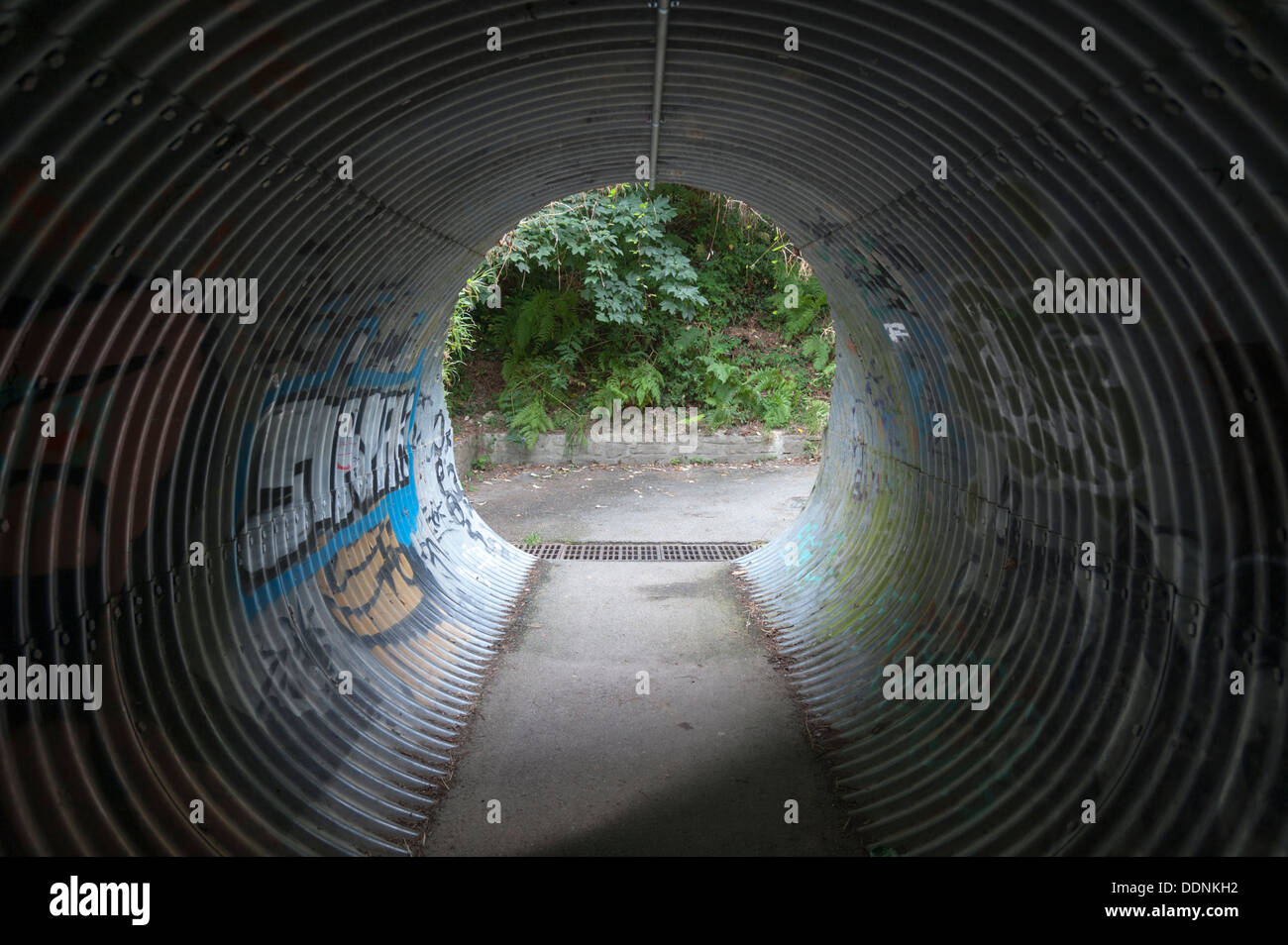 Un ferro corrugato sottopassaggio tunnel con graffiti dipinti sui muri Foto Stock