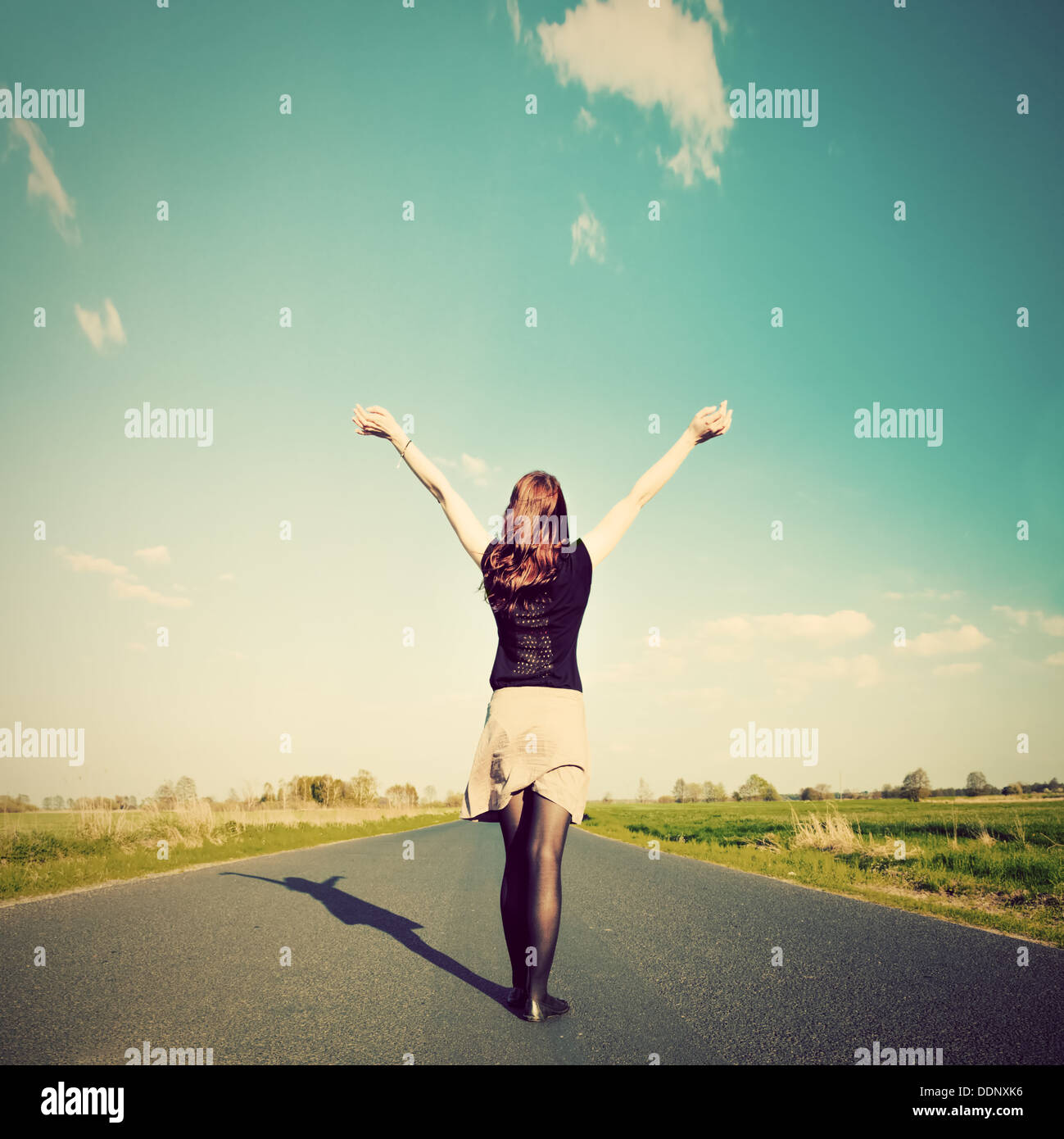 Donna felice in piedi con le mani in alto sulla strada diritta rivolta verso il sole. Futuro / libertà / speranza / concetto di successo Foto Stock