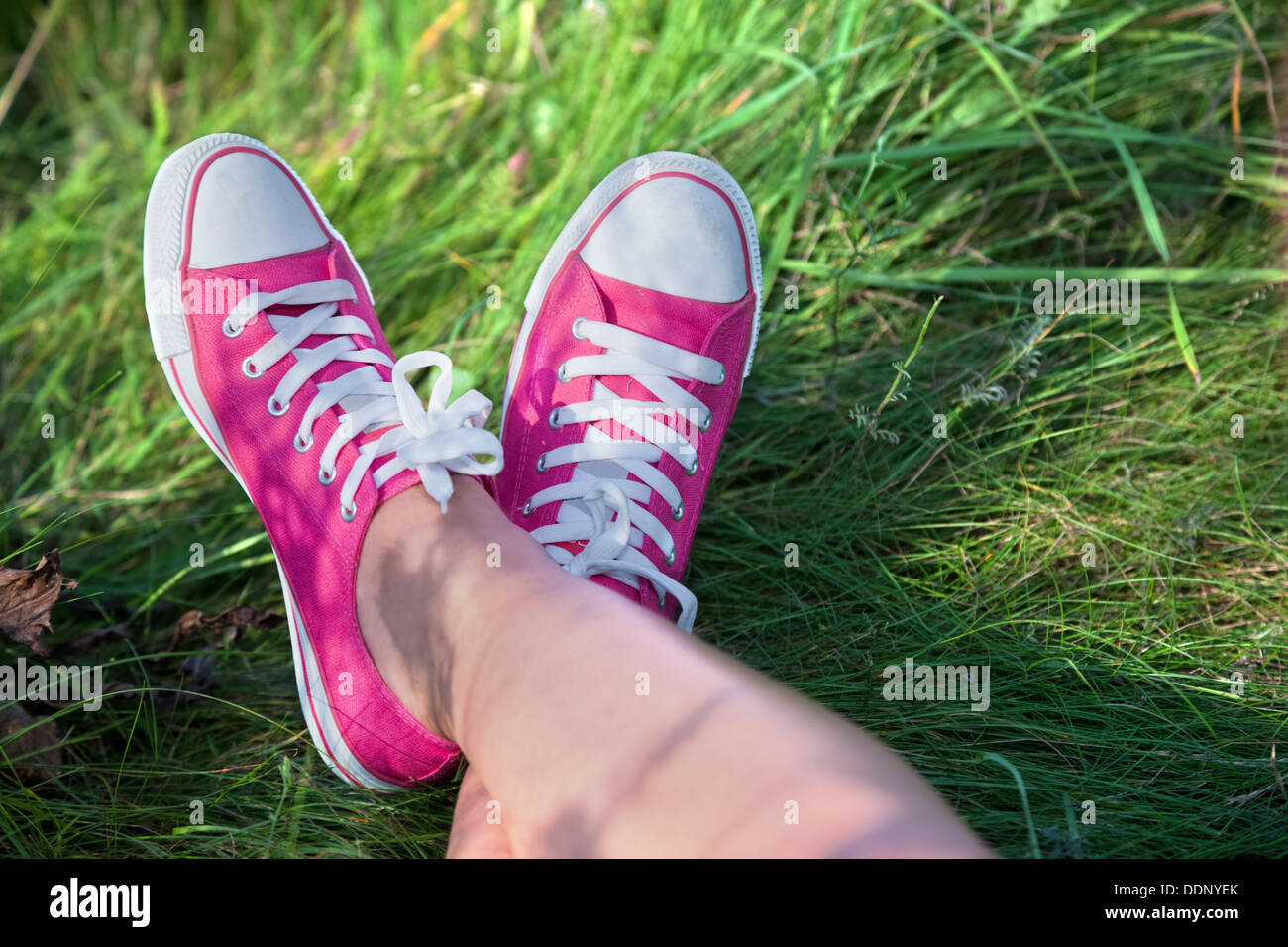 Donna che indossa formatori di colore rosa con le gambe incrociate al di fuori - punti di vista Foto Stock