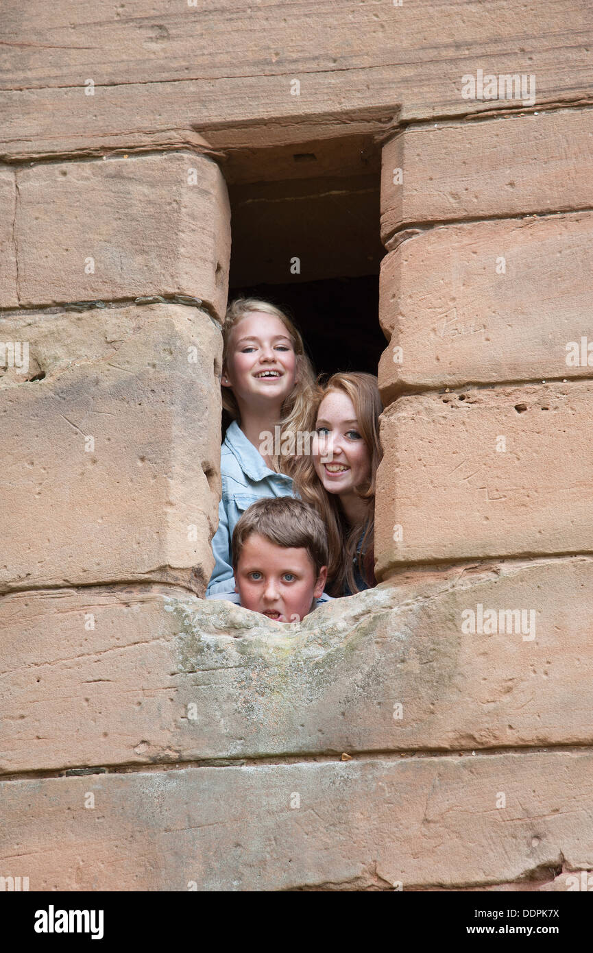 Tre bambini di guardare attraverso una finestra glassless Foto Stock