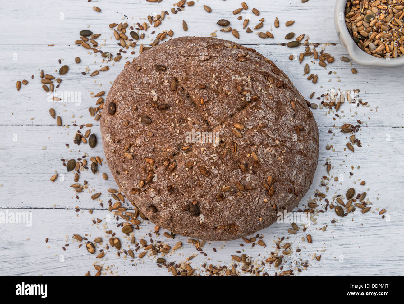 Pane di segale con semi sparsi intorno ad esso su bianco tavola di legno Foto Stock
