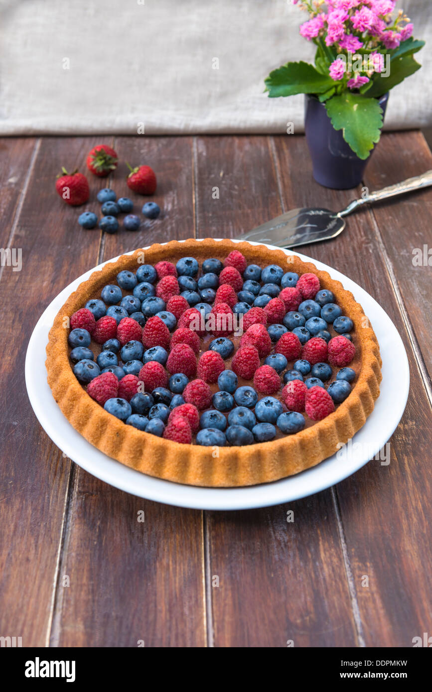 Una torta guarnita con frutta estiva - lamponi e mirtilli sul tavolo di legno Foto Stock