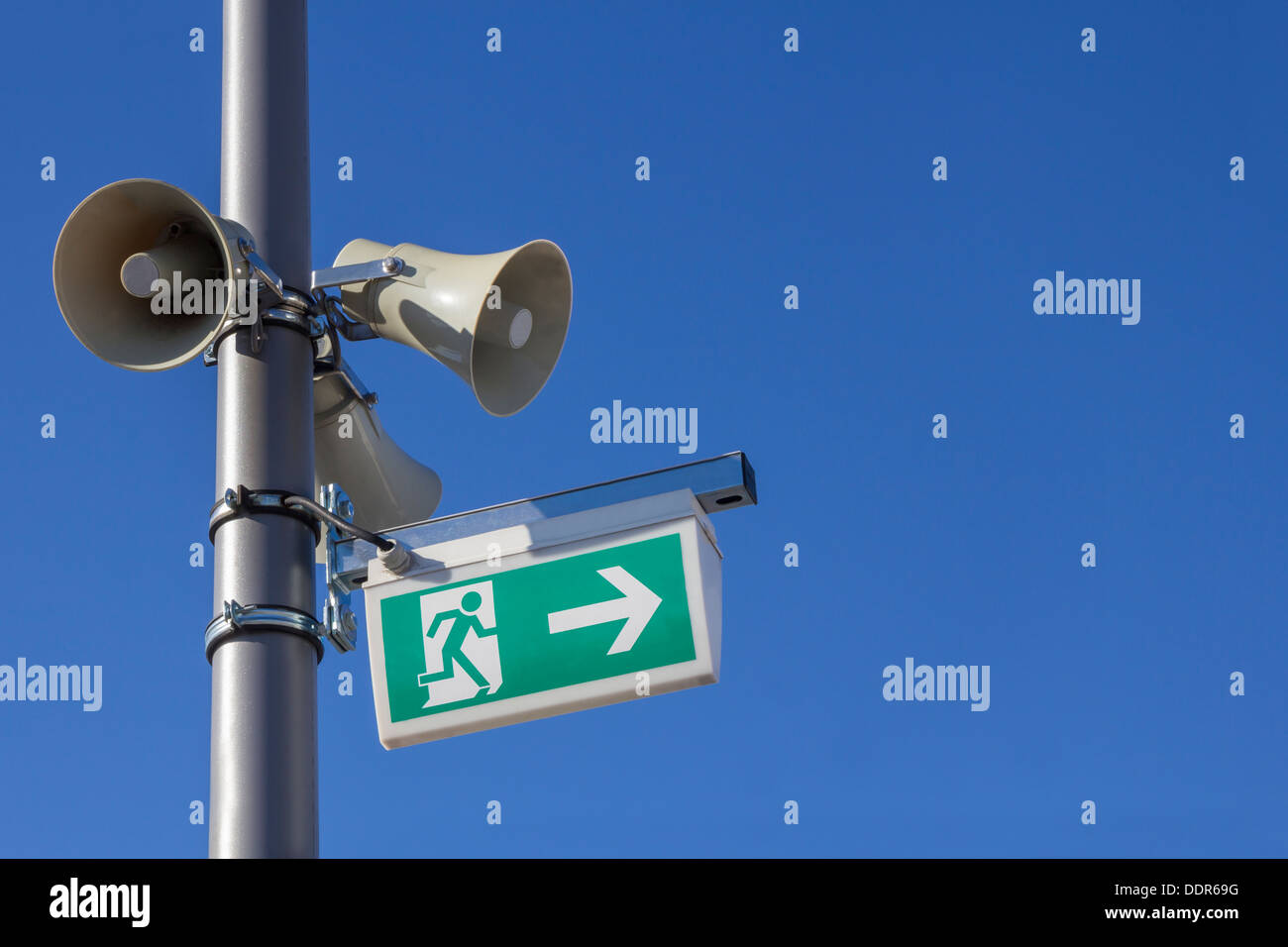Tre i megafoni e una uscita di emergenza segno montato su un palo di argento sul blu del cielo Foto Stock