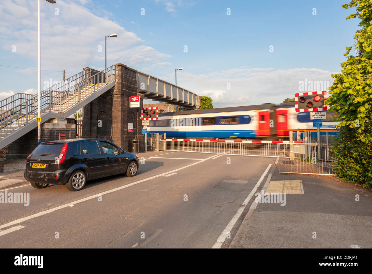 Auto in attesa ad un passaggio a livello con barriere abbassate come un treno che passa. Attenborough stazione ferroviaria, Nottinghamshire, England, Regno Unito Foto Stock