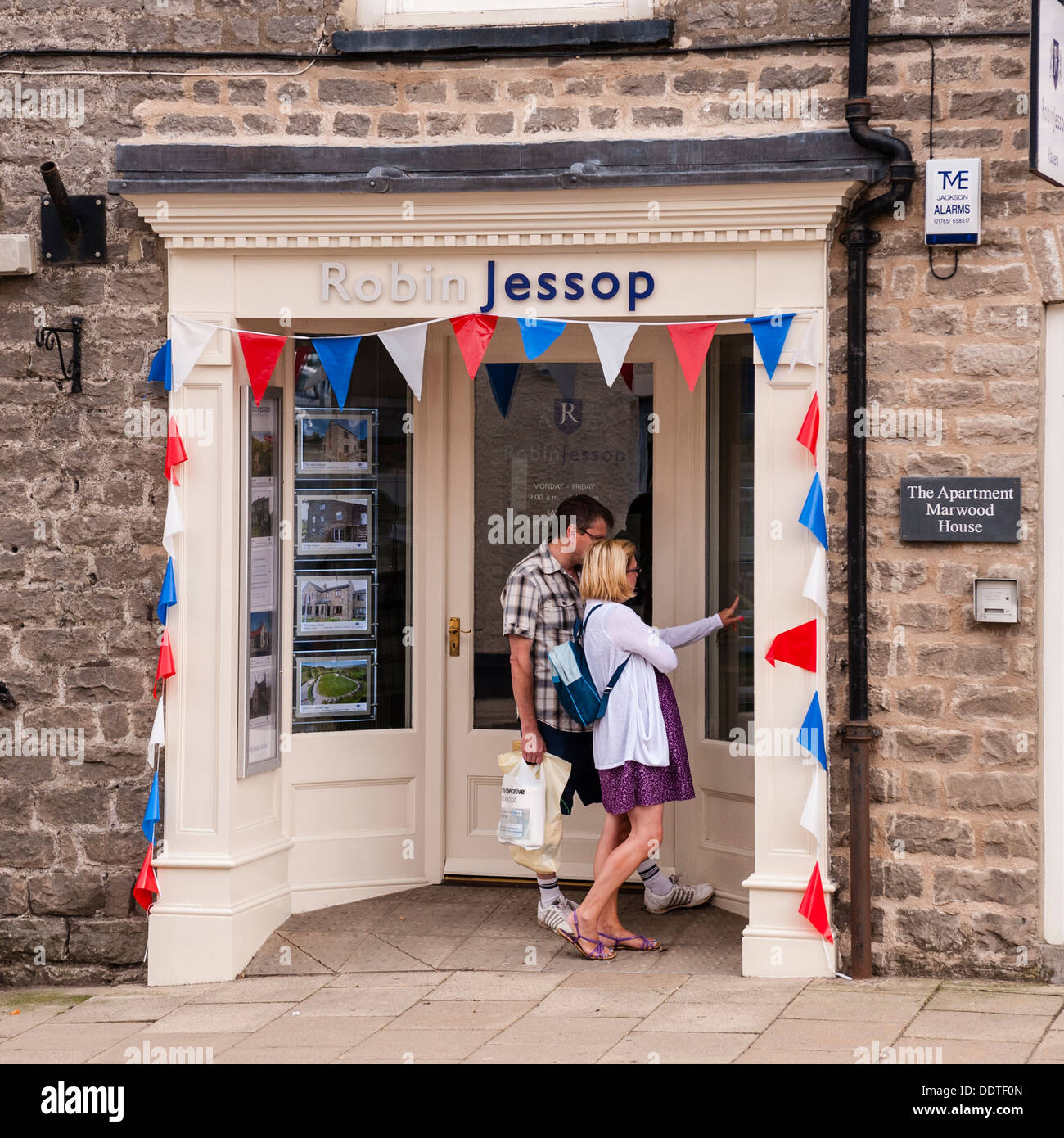 Una giovane coppia in cerca nella finestra della Robin Jessop agenti immobiliari in Leyburn , North Yorkshire , Inghilterra , Inghilterra , Regno Unito Foto Stock