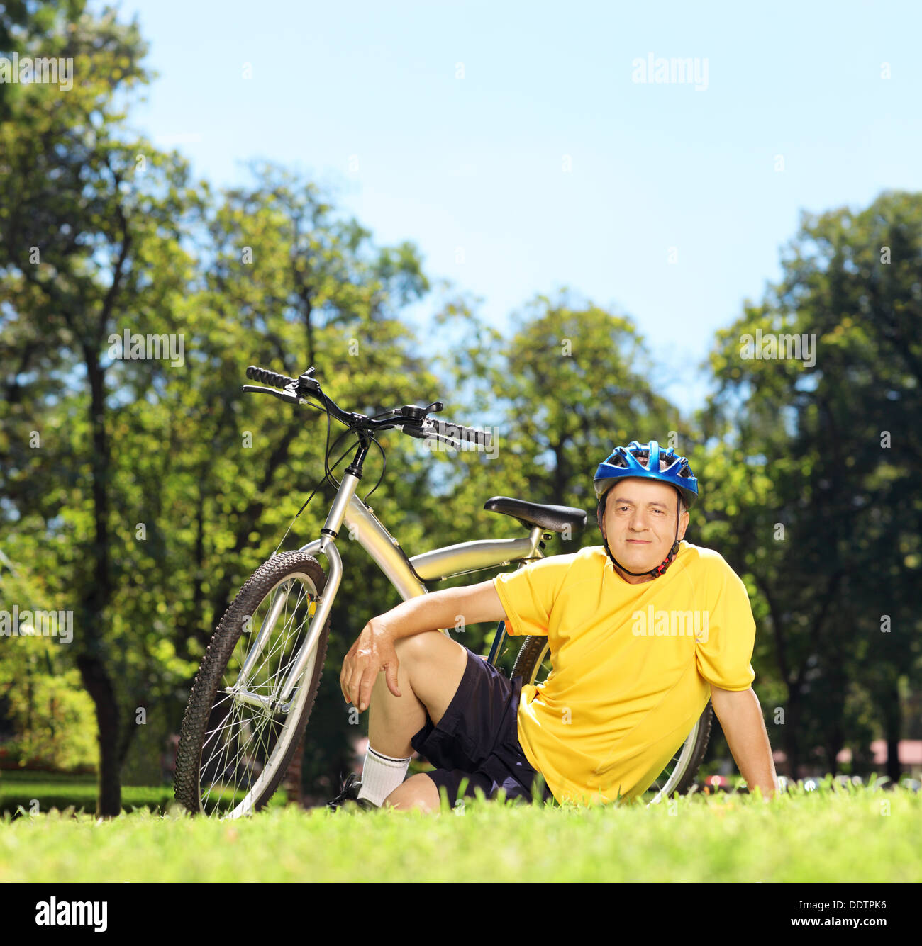 Uomo maturo in sportswear seduto su un vetro verde vicino alla sua bicicletta in un parco Foto Stock