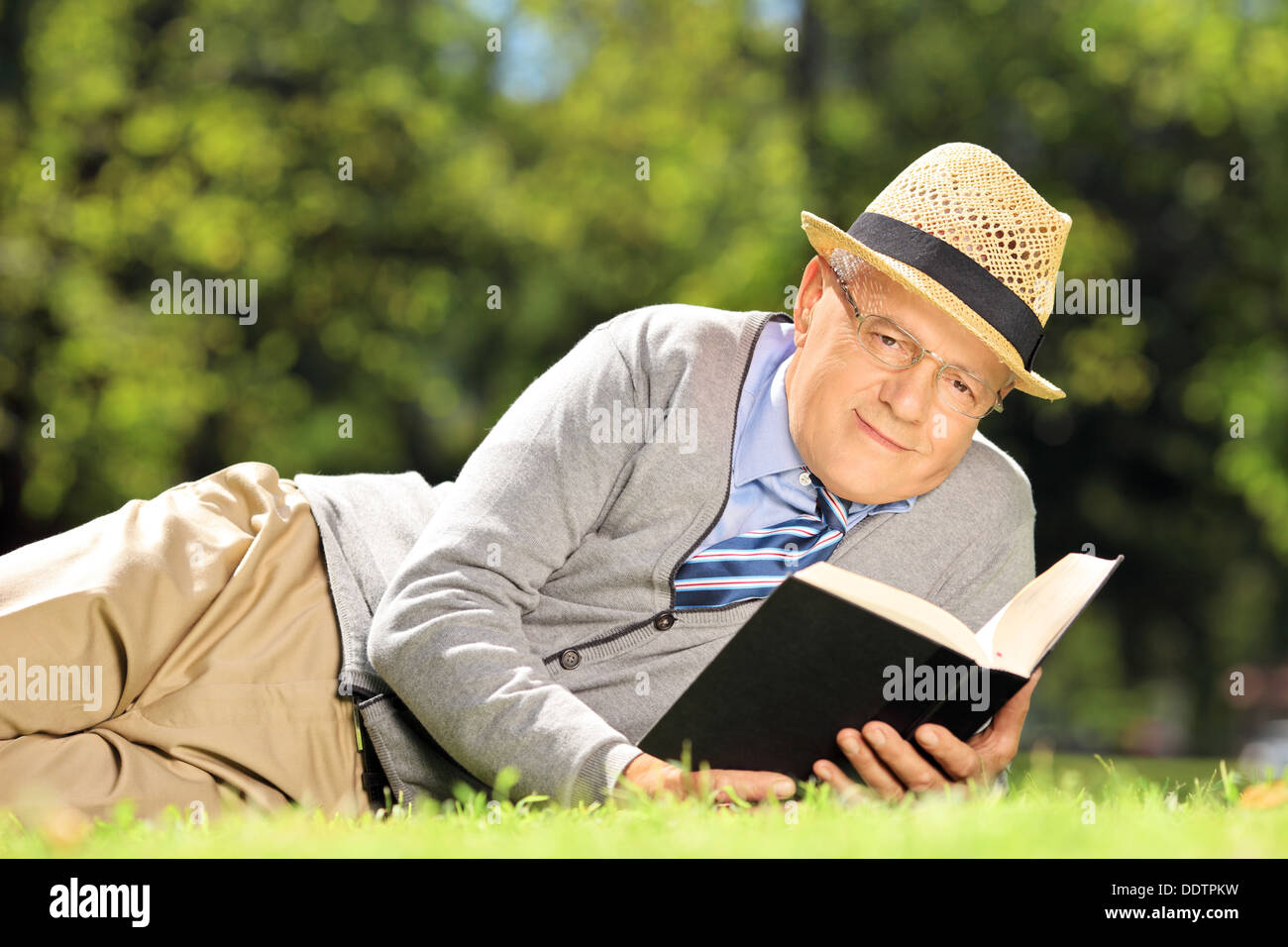 Senior gentleman sdraiati su un prato con un libro in posizione di parcheggio Foto Stock