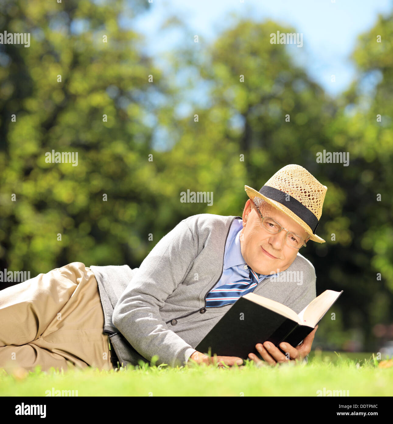 Senior gentleman sdraiati su un prato con un libro in posizione di parcheggio Foto Stock
