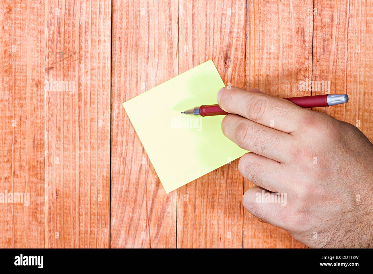 Nota vuota, carta stick, mano d'uomo in possesso di una penna, su uno sfondo di legno. Foto Stock