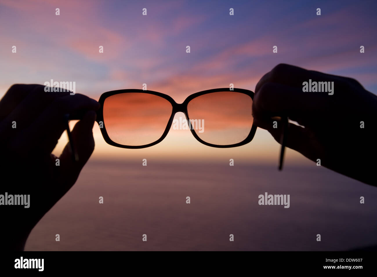 Anonimo holiday maker tiene gli occhiali da sole fuori contro un tramonto sul mare a Mallorca, Spagna. Foto Stock