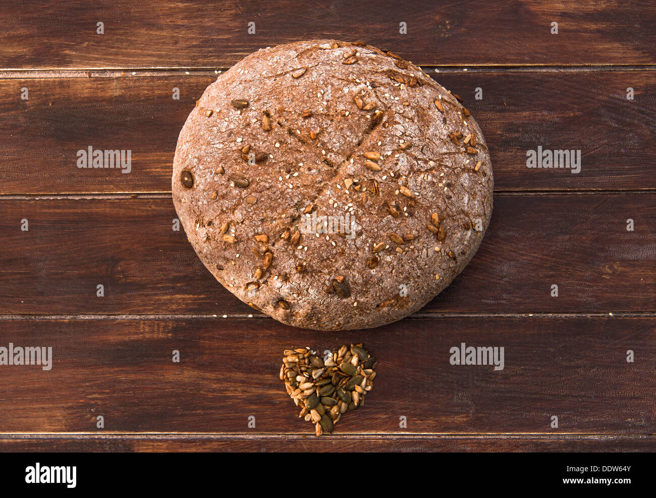 Home cotto il pane integrale con semi sparsi intorno ad esso su un tavolo di legno Foto Stock