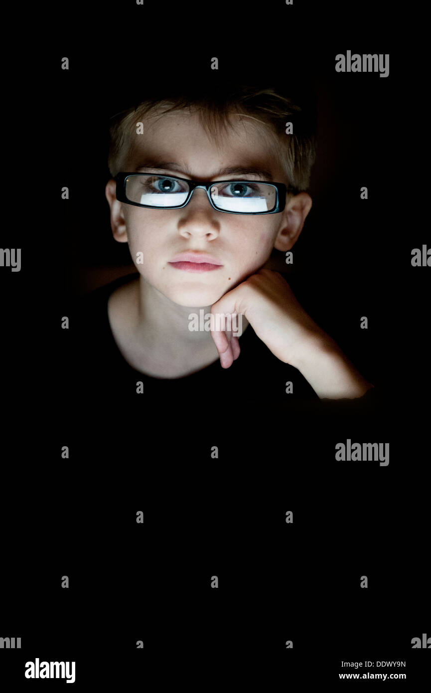 Un ragazzo guarda la fotocamera in una stanza buia con il viso illuminato da uno schermo di computer Foto Stock