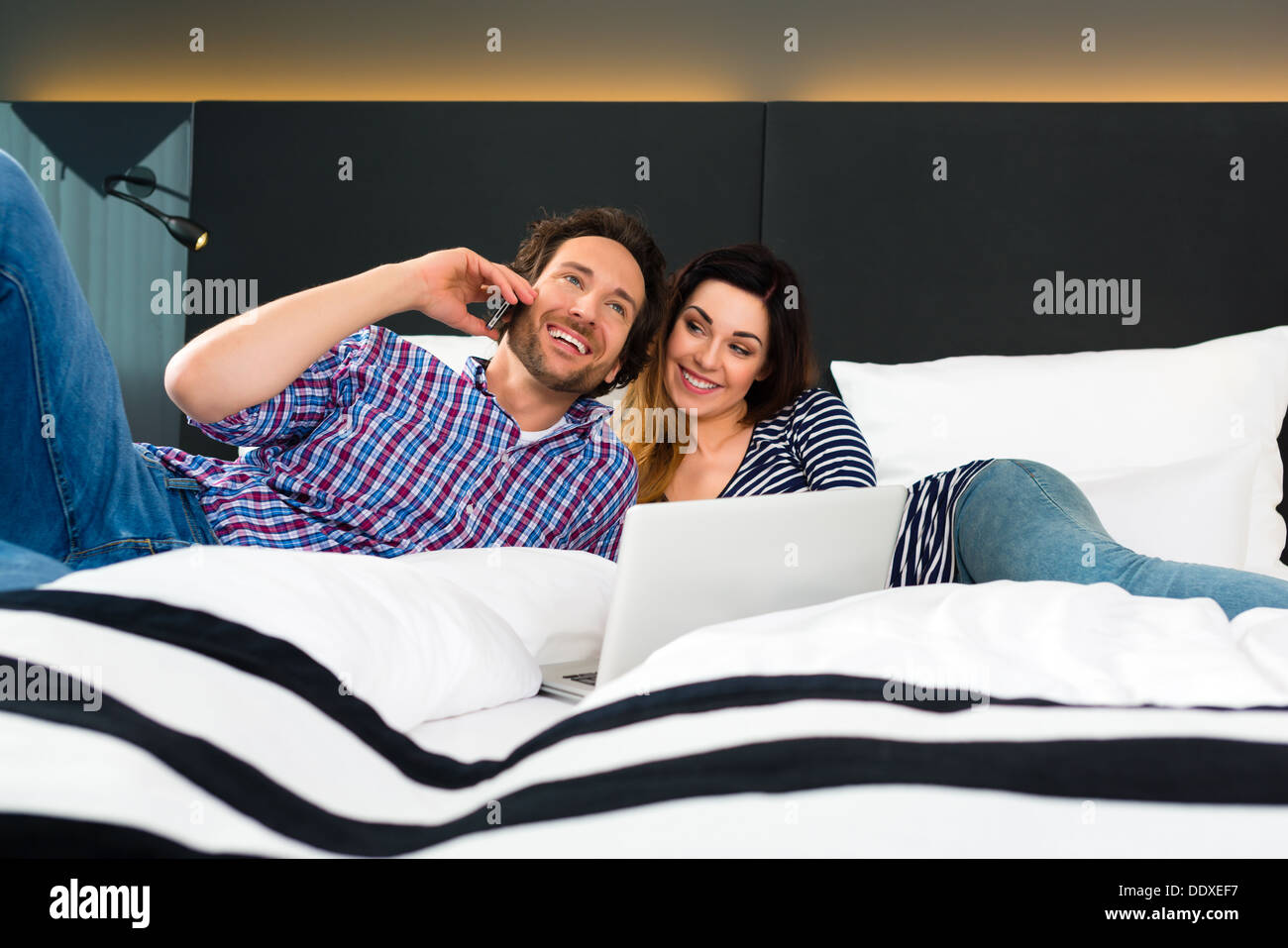 Coppia giovane sdraiato sul letto di una camera di albergo suite, sono in  vacanza e usando il wifi in camera Foto stock - Alamy
