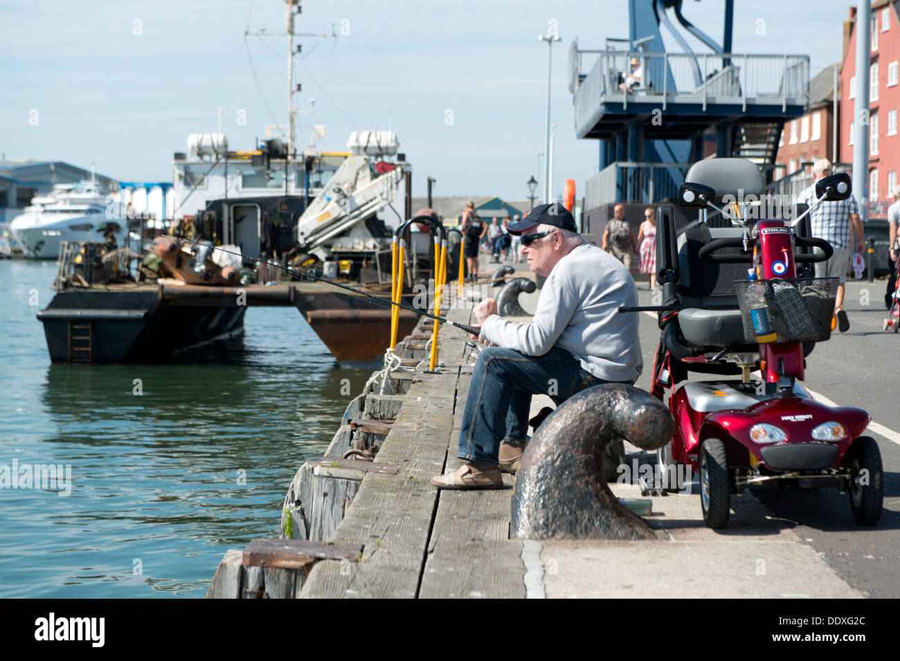 Titolare di una pensione o di una rendita si siede la pesca dalla banchina in Poole nella contea del Dorset in Inghilterra del sud. Foto Stock