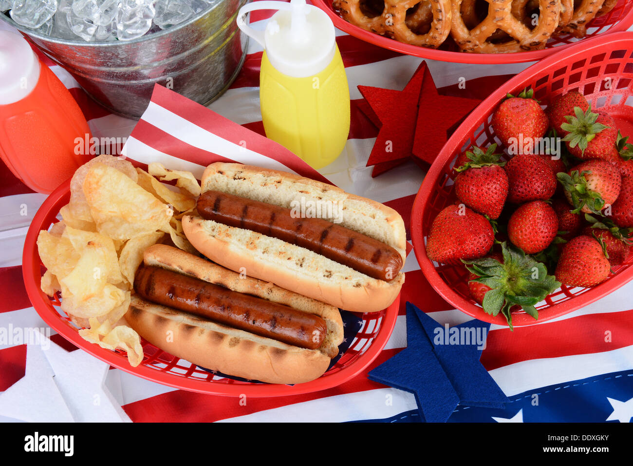 Guardando in giù su un tavolo da picnic decorato per il 4 di luglio. Hot Dogs, patatine, fragole, senape, ketchup. Foto Stock