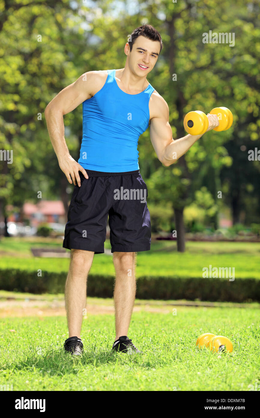 A piena lunghezza Ritratto di un atleta sorridente esercitando con peso in un parco Foto Stock