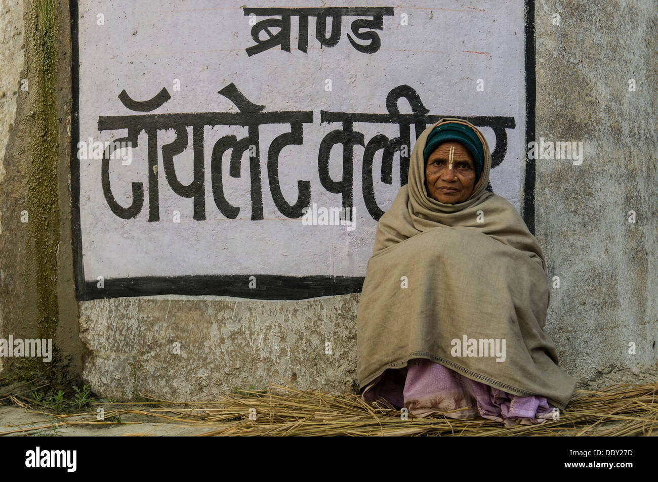 Donna seduta in corrispondenza di una parete con la scrittura in lingua Hindi, durante il Kumbha Mela Foto Stock
