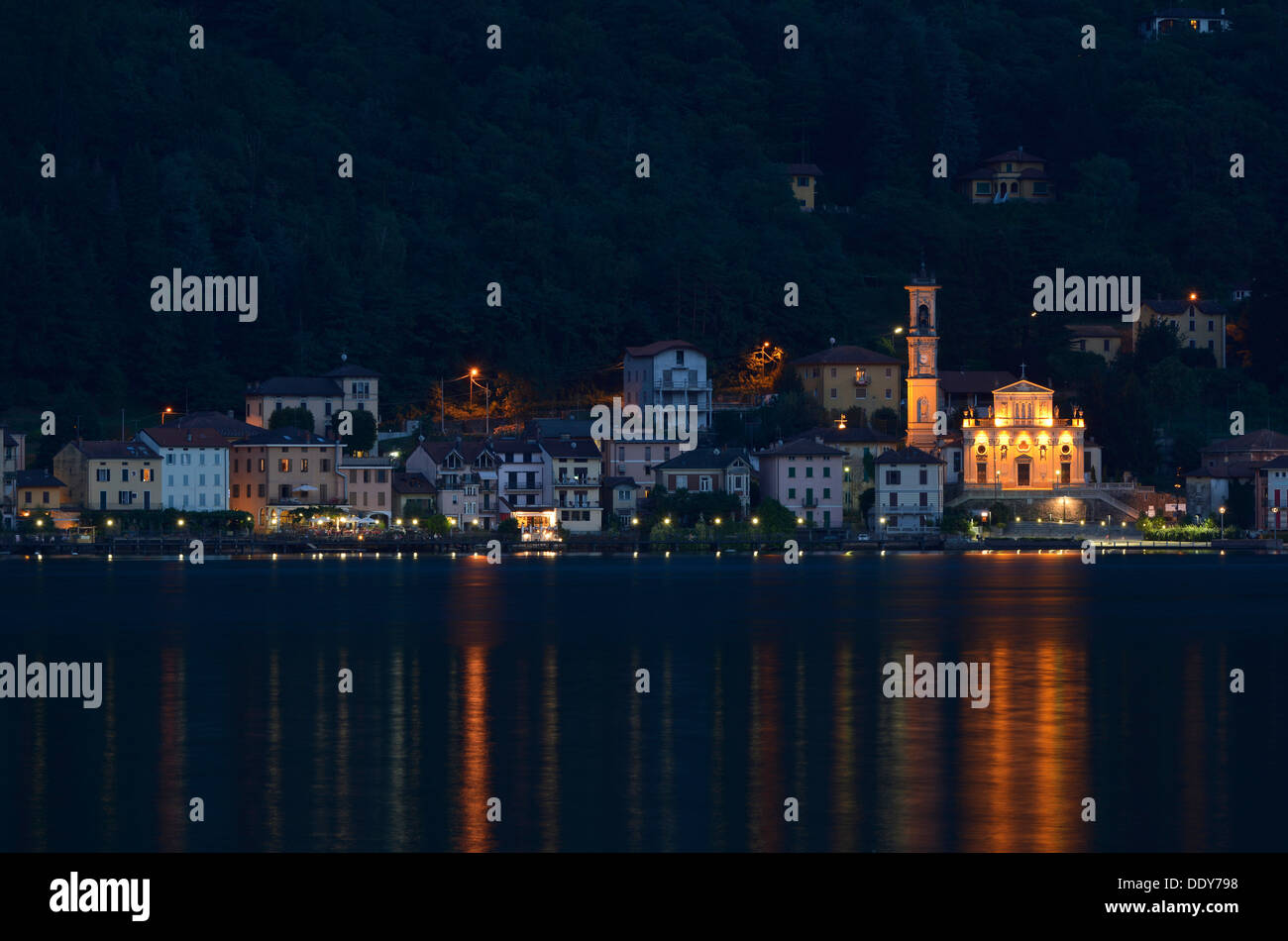 Villaggio di Porto Ceresio con la chiesa parrocchiale della Chiesa Sancto Ambrosio sul Lago di Lugano o Lago di Lugano di notte Foto Stock