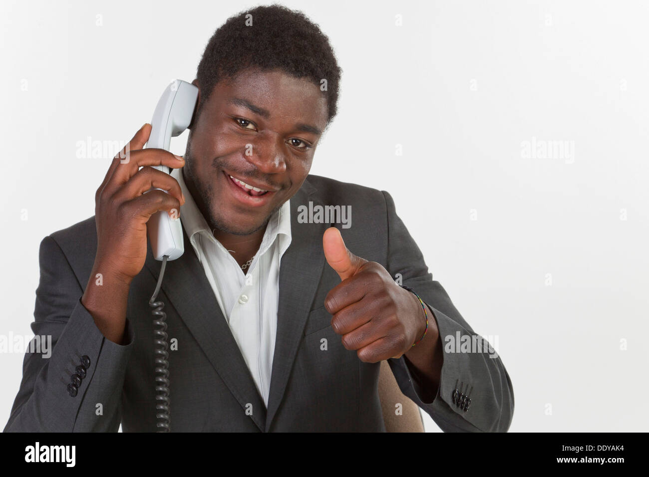Giovane uomo nero in una tuta facendo una telefonata in un ufficio, sorridente con il pollice in alto gesto Foto Stock
