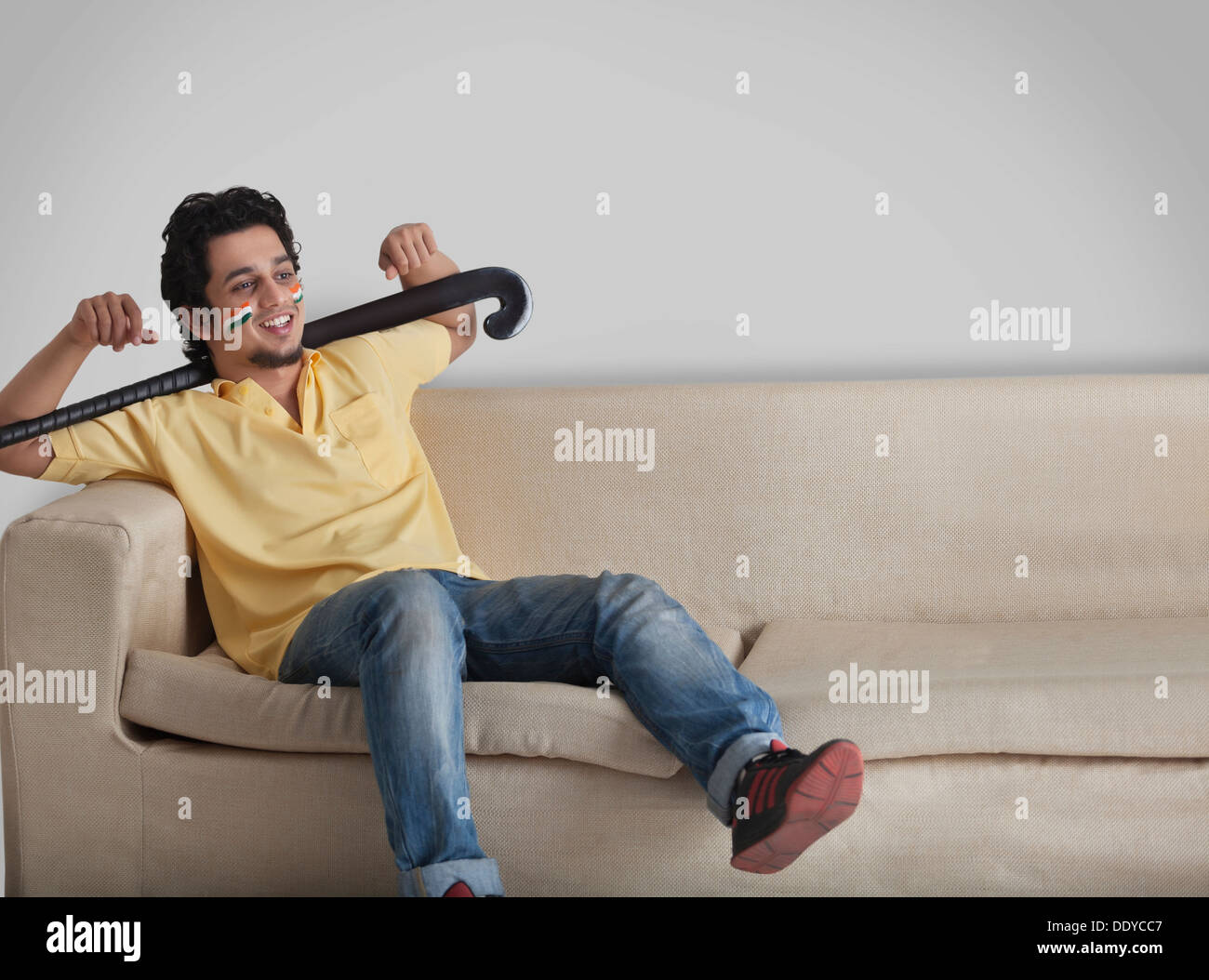 Giovane casuals sul divano guardando lontano tenendo mazza da hockey Foto Stock