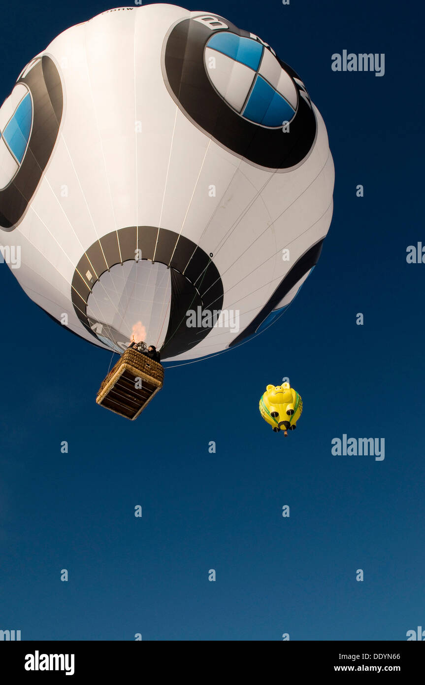 Due i palloni ad aria calda fino al cielo, una BMW con loghi e un palloncino giallo nella forma di un maiale sorridente xii balloon festival Foto Stock