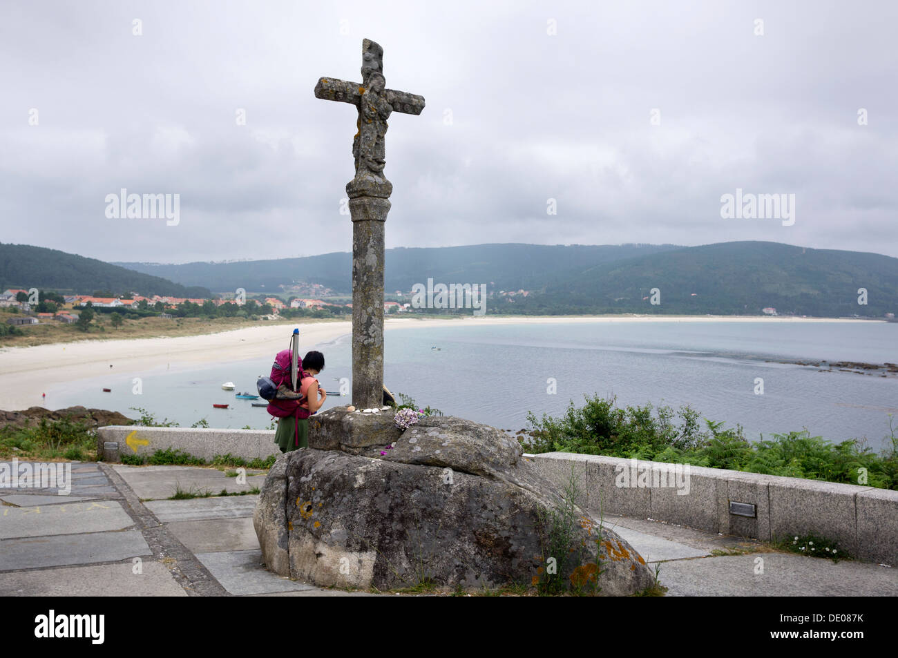 Un pellegrino mostra una delle spiagge in Finisterre accanto a uno della croce di pietra del cammino di san Giacomo. Foto Stock