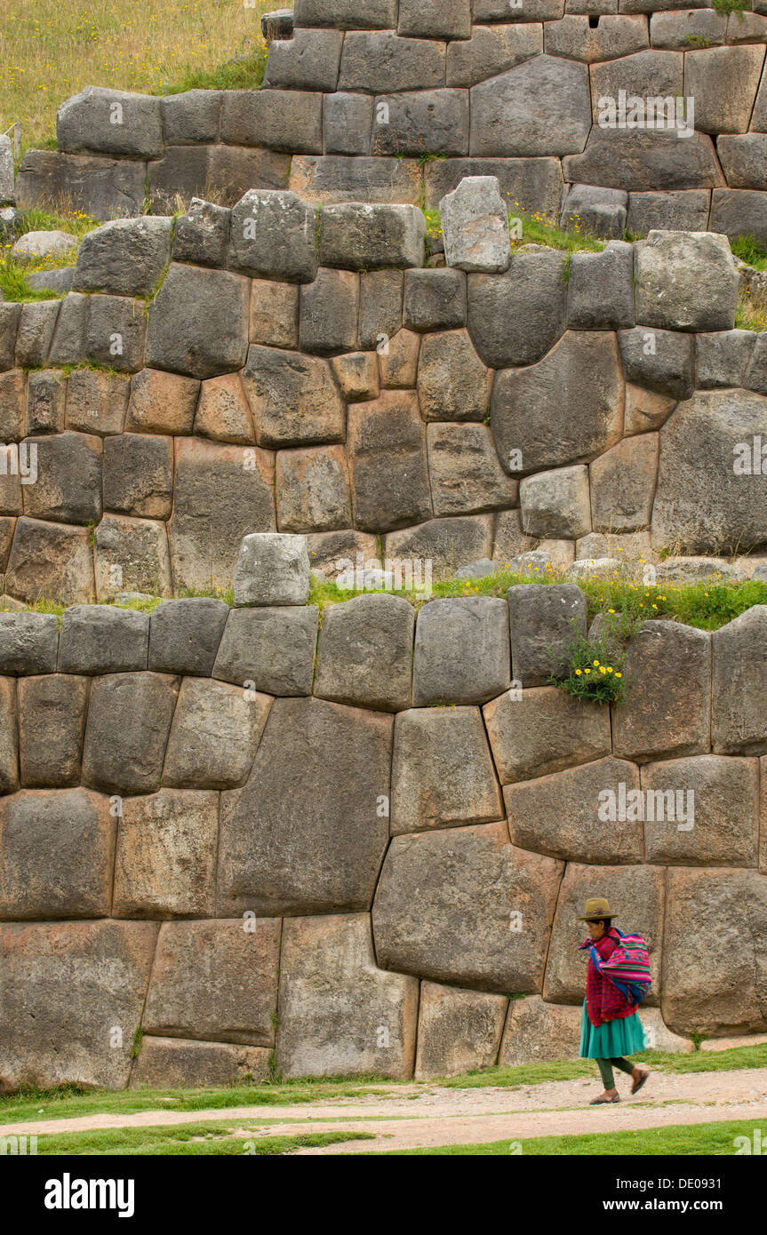 La donna nel tradizionale abito andina e hat, passato a piedi di fissaggio a parete a schiera di pietre di incastro, Saksaywaman, Cusco, Perù Foto Stock
