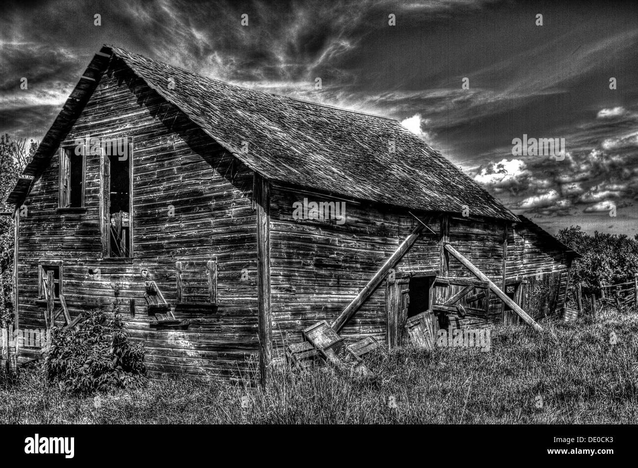 Un HDR, foto in bianco e nero di un vecchio rustico capannone di legno contro il drammatico guardando il cielo. Foto Stock