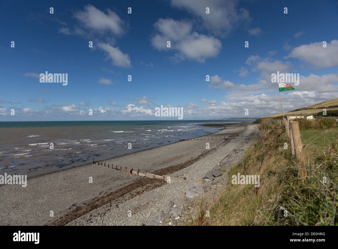 Spiaggia ghiaiosa e Ceredigion sentiero costiero a Aberarth, il Galles Centrale, con il gallese drago rosso bandiera soffia nel forte vento onshore. Foto Stock