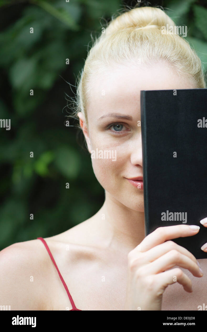 Giovane donna libro di contenimento nella parte anteriore del viso, ritratto Foto Stock