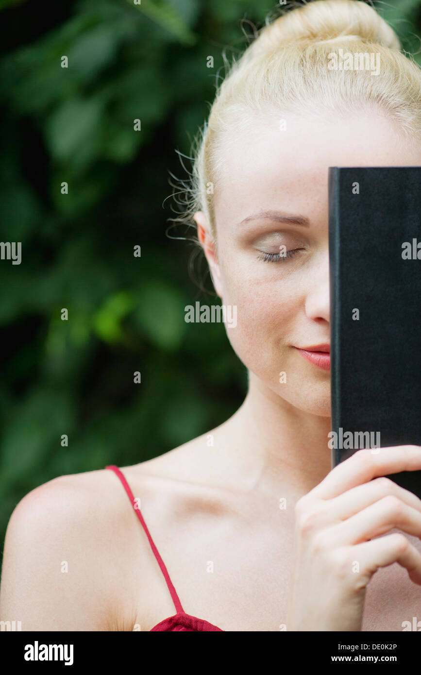 Giovane donna libro di contenimento nella parte anteriore del volto a occhi chiusi Foto Stock