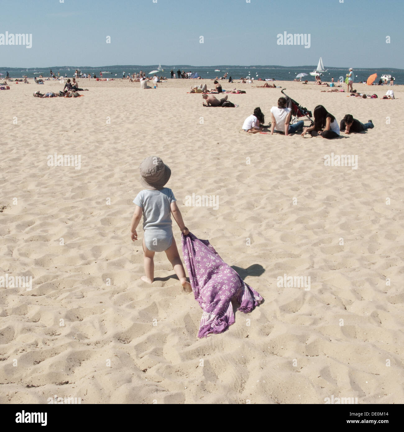 Infant camminando sulla spiaggia, trascinando una coperta dietro di lui Foto Stock